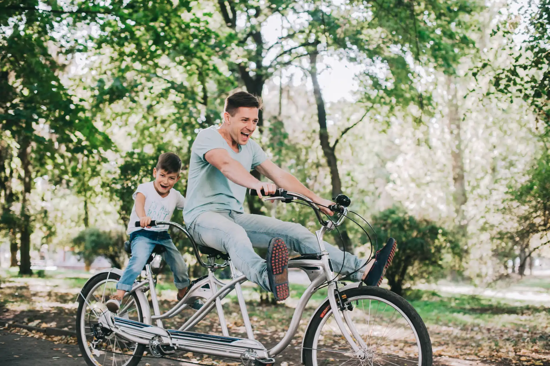 Homem e menino andam de bicicleta em um parque, sorrindo e se divertindo.