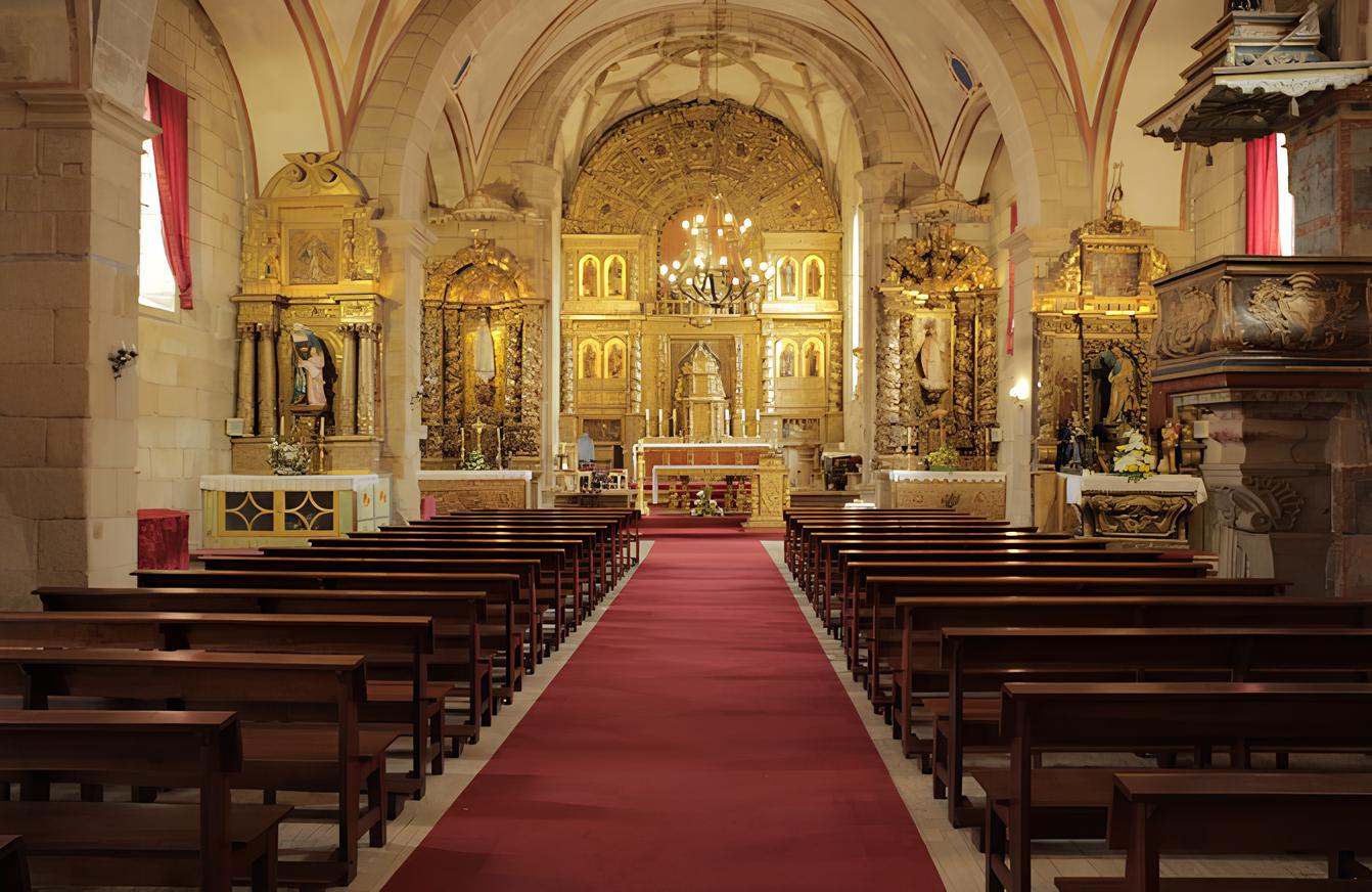 Interior de uma igreja com altar dourado, bancos de madeira e carpete vermelho no corredor central.