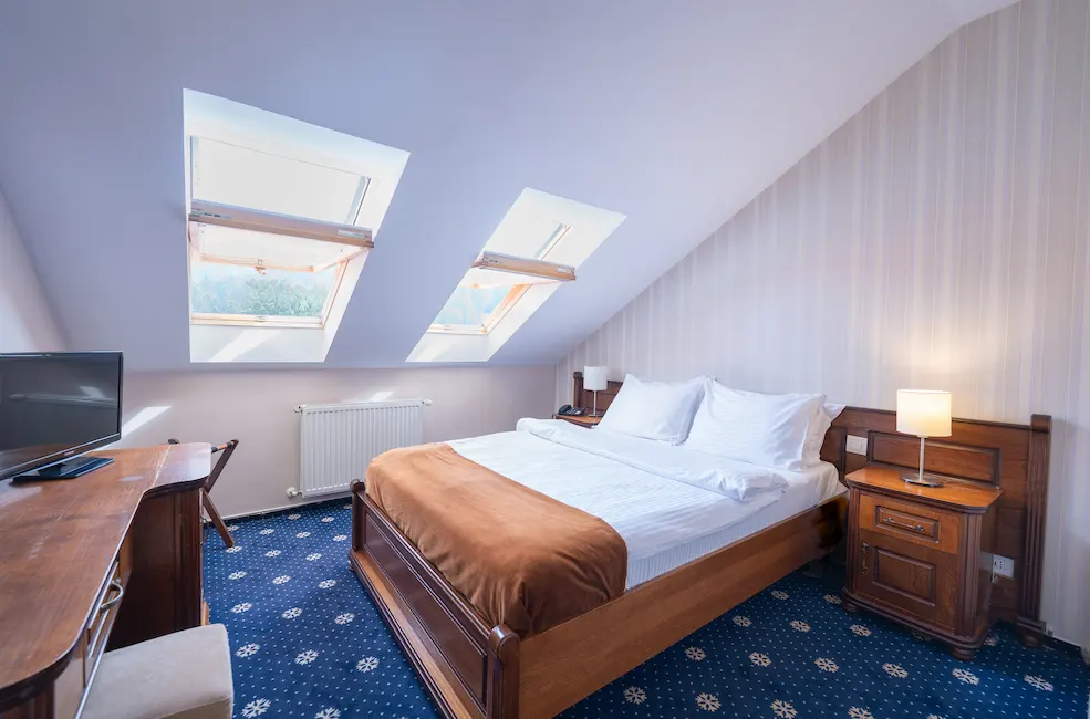Cozy attic bedroom with skylight, bed, desk, and lamp.