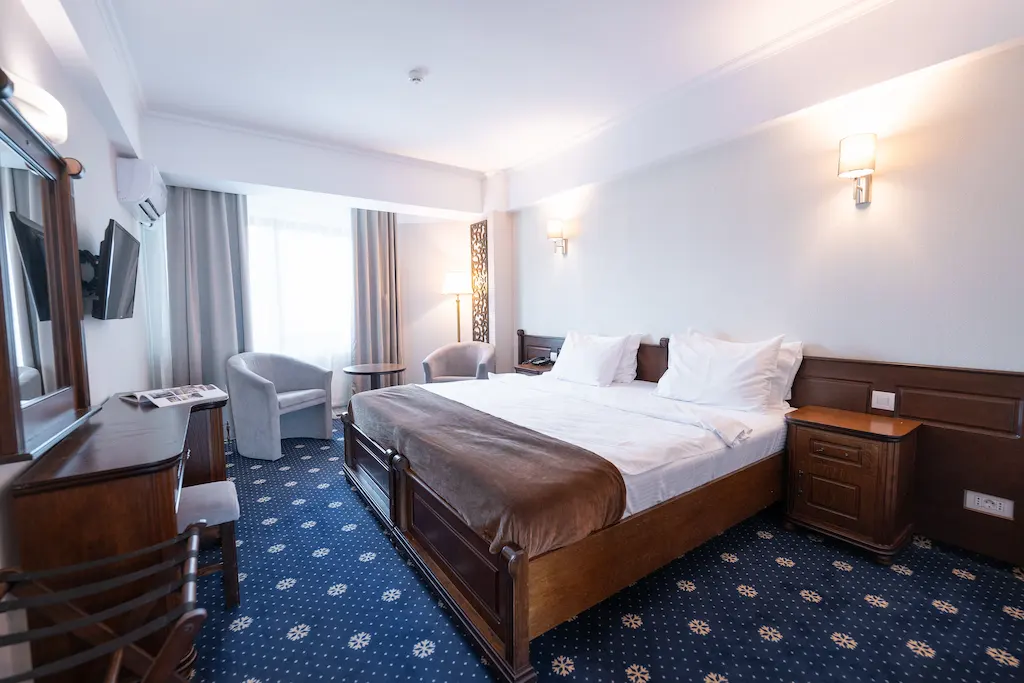 Hotel room with a double bed, armchairs, and a TV.