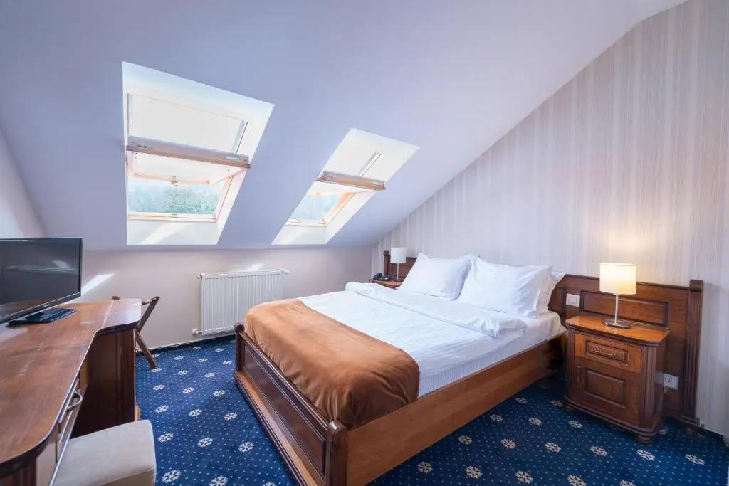 Cozy attic bedroom with skylights, wooden furniture, and blue carpet.