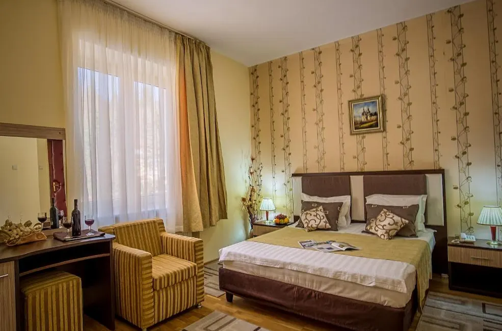 Cozy hotel room with a bed, striped armchair, desk, and decorative wallpaper.