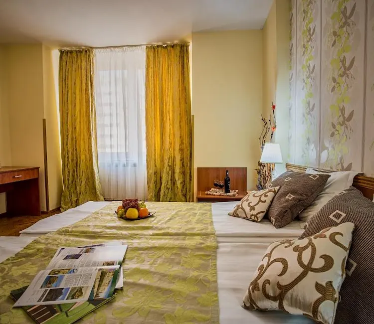 Cozy bedroom with patterned pillows, fruit bowl, and large window with curtains.