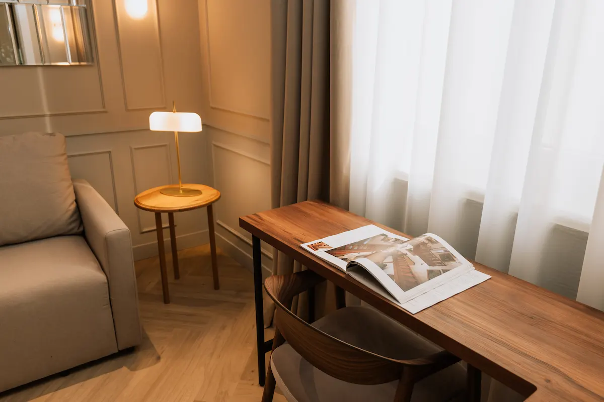 Cozy room with a sofa, side table, lamp, and wooden desk by a window.
