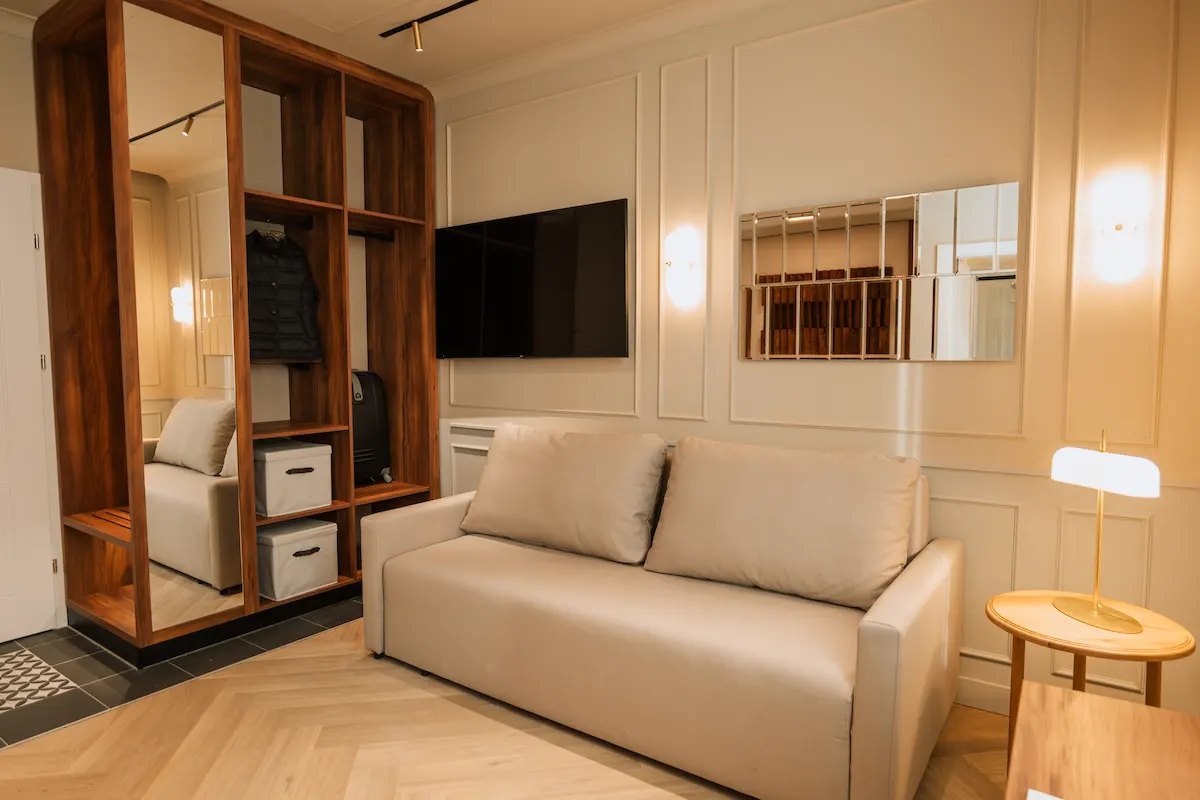 Modern living room with a beige sofa, wooden shelves, and a mounted TV.