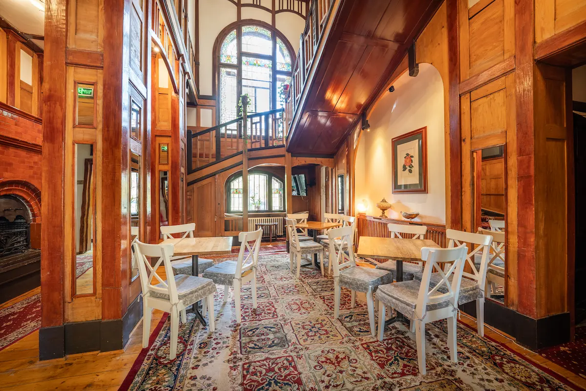 Cozy room with wooden decor, chairs, tables, and a staircase.