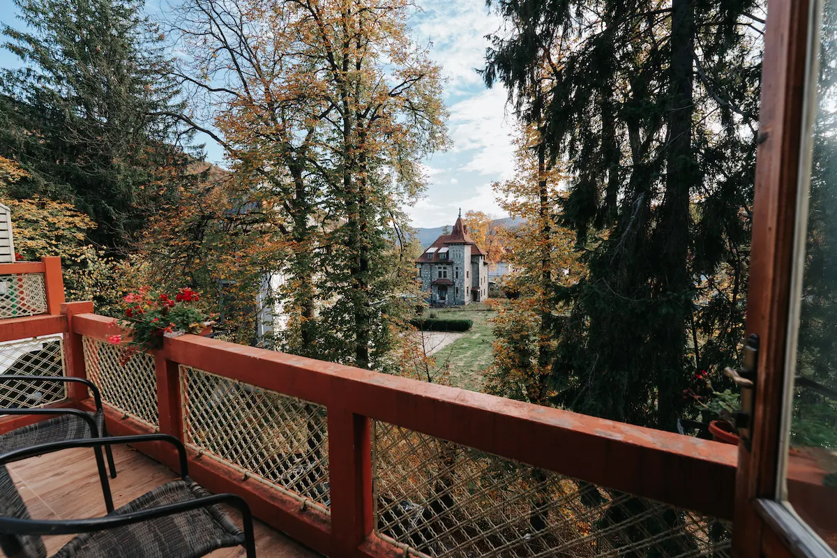 View of a house through autumn trees from a wooden balcony with chairs.