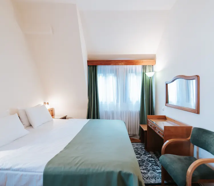 Cozy hotel room with a bed, desk, and chair by a window.
