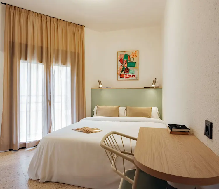 Habitaci&oacute;n minimalista con cama doble, escritorio y decoraci&oacute;n colorida en la pared.