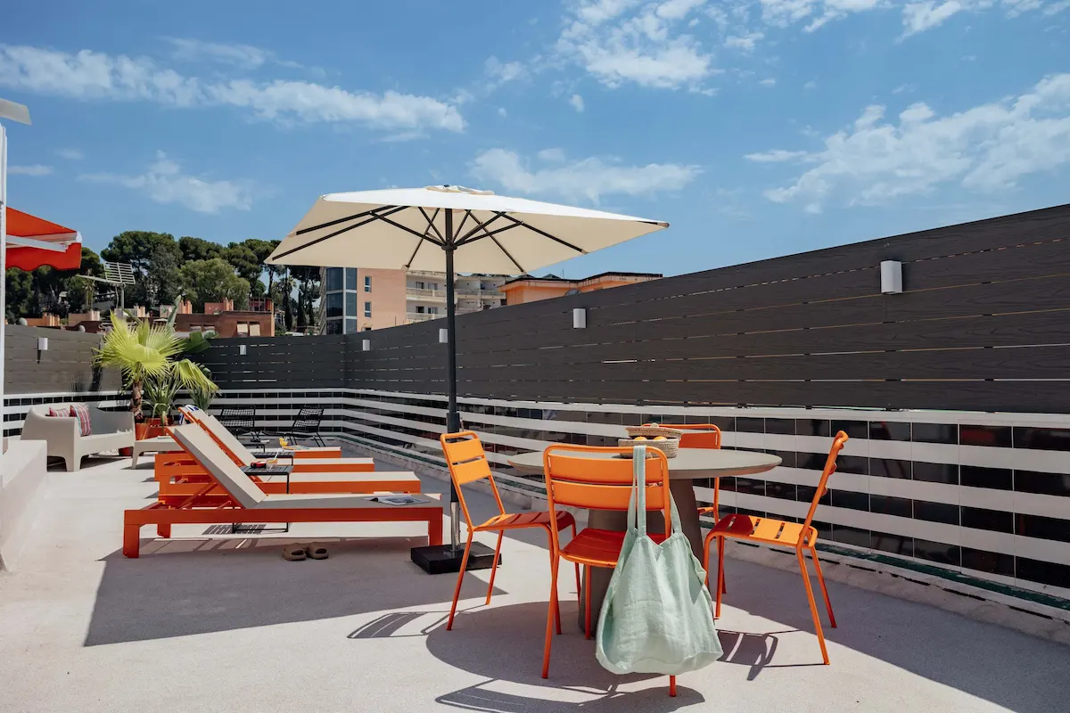 Terraza con sillas y sombrilla bajo un cielo azul.