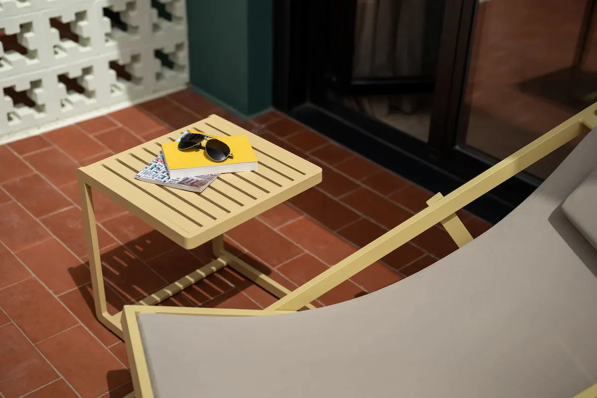 Mesa con gafas de sol, revistas y libro amarillo junto a una silla en terraza.