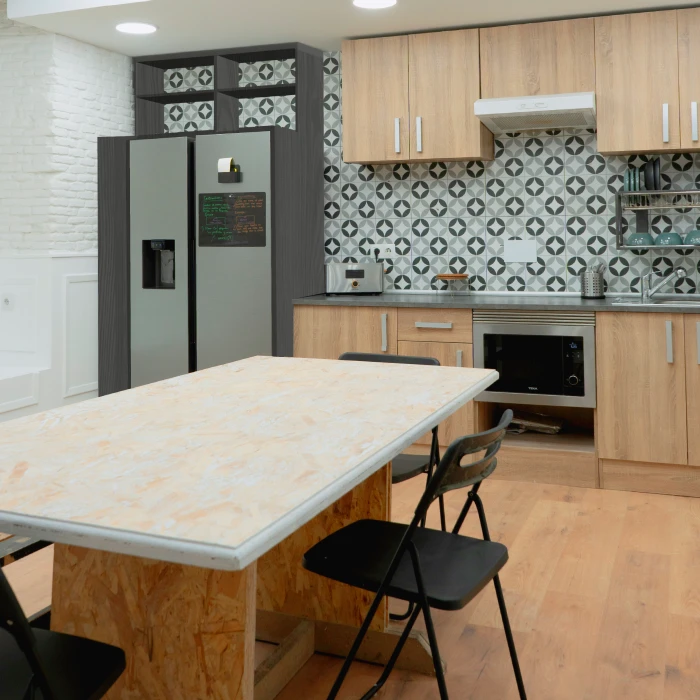 Cocina moderna con mesa de madera, sillas negras y fondo de azulejos geom&eacute;tricos.