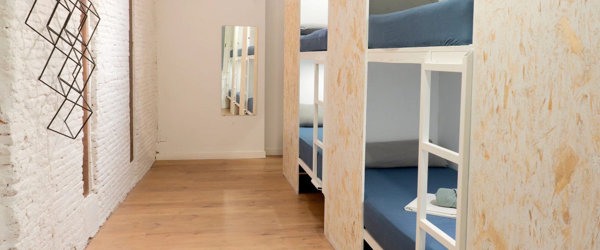 Literas en un dormitorio moderno con pared de ladrillo blanco y suelo de madera.