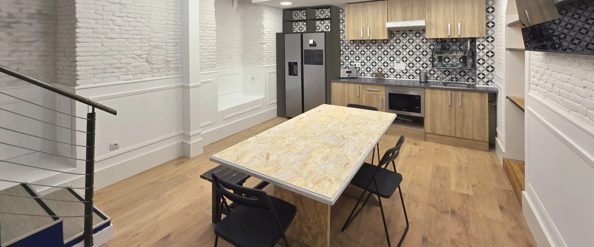 Cocina moderna con mesa de madera, sillas negras y azulejos decorativos.