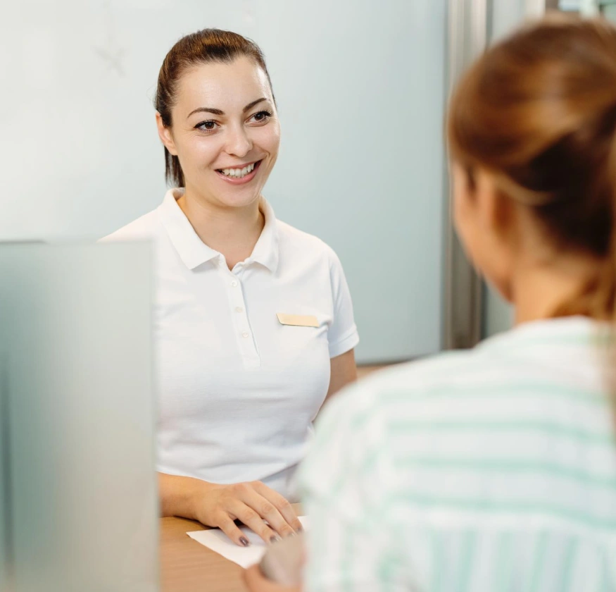 Persona sonriente atendiendo a cliente en mostrador de recepci&oacute;n.