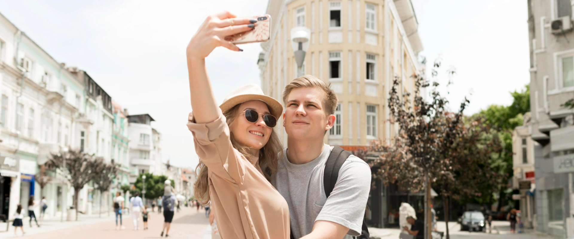Pareja tom&aacute;ndose una selfie en una calle soleada.