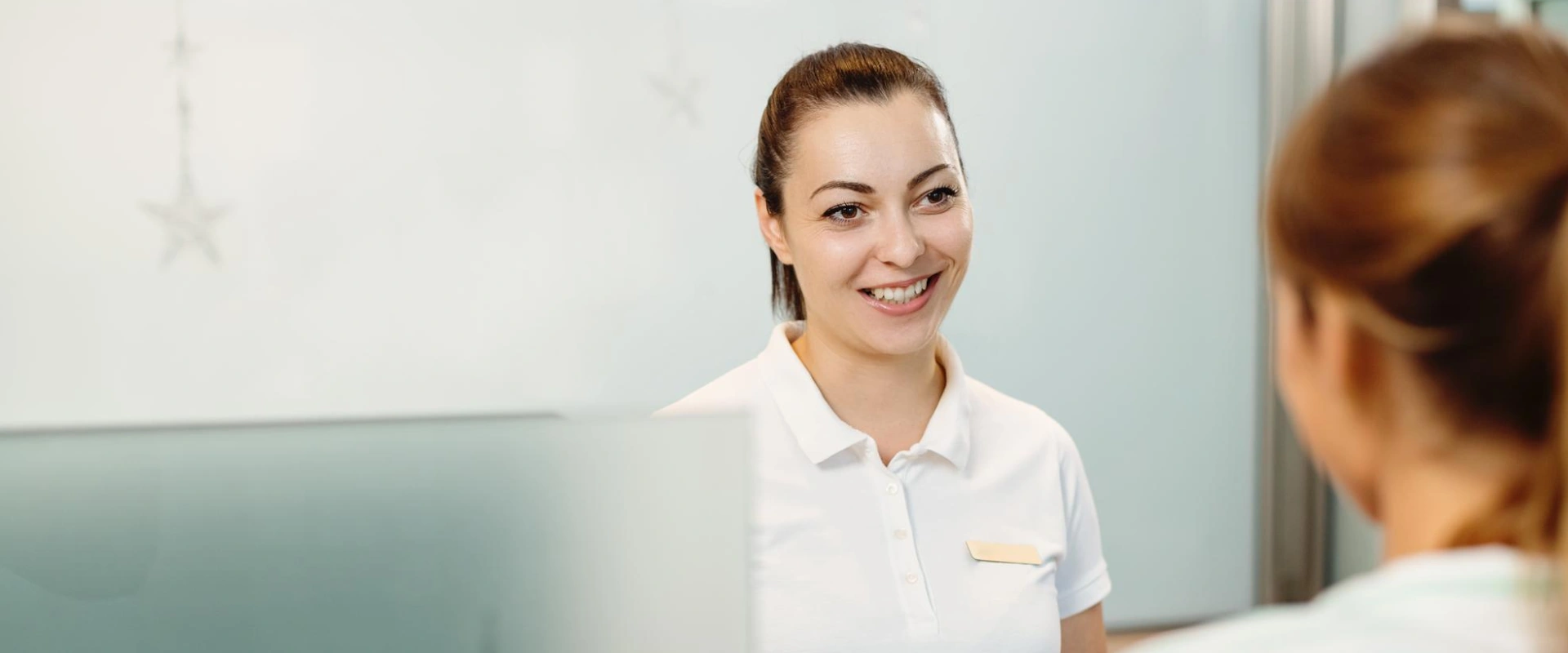 Mujer sonriente de uniforme blanco conversando con otra persona.