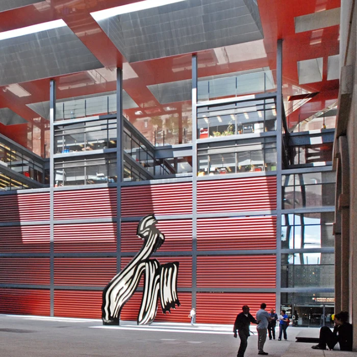 Fachada moderna roja con escultura abstracta y personas caminando.