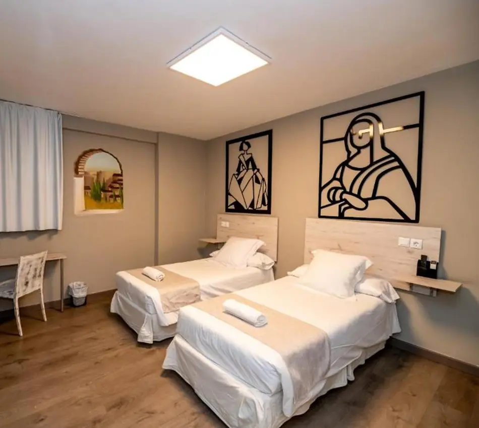 Habitaci&oacute;n con dos camas, decorada con cuadros y escritorio junto a la ventana.