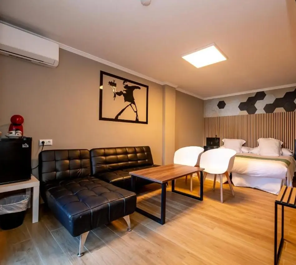 Sala moderna con sof&aacute; negro, cama matrimonial y mesa de madera.