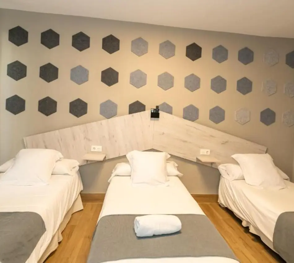 Tres camas individuales con cabeceras triangulares y pared decorada con hex&aacute;gonos.