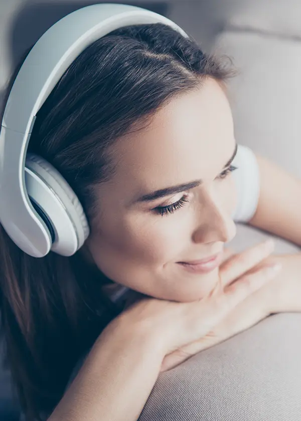 Mujer con auriculares blancos sonriendo y apoyada en un sof&aacute;.