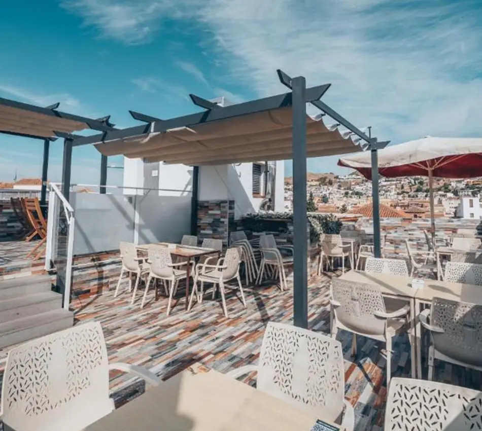 Terraza con sillas y mesas bajo toldos, vista panor&aacute;mica de ciudad al fondo.