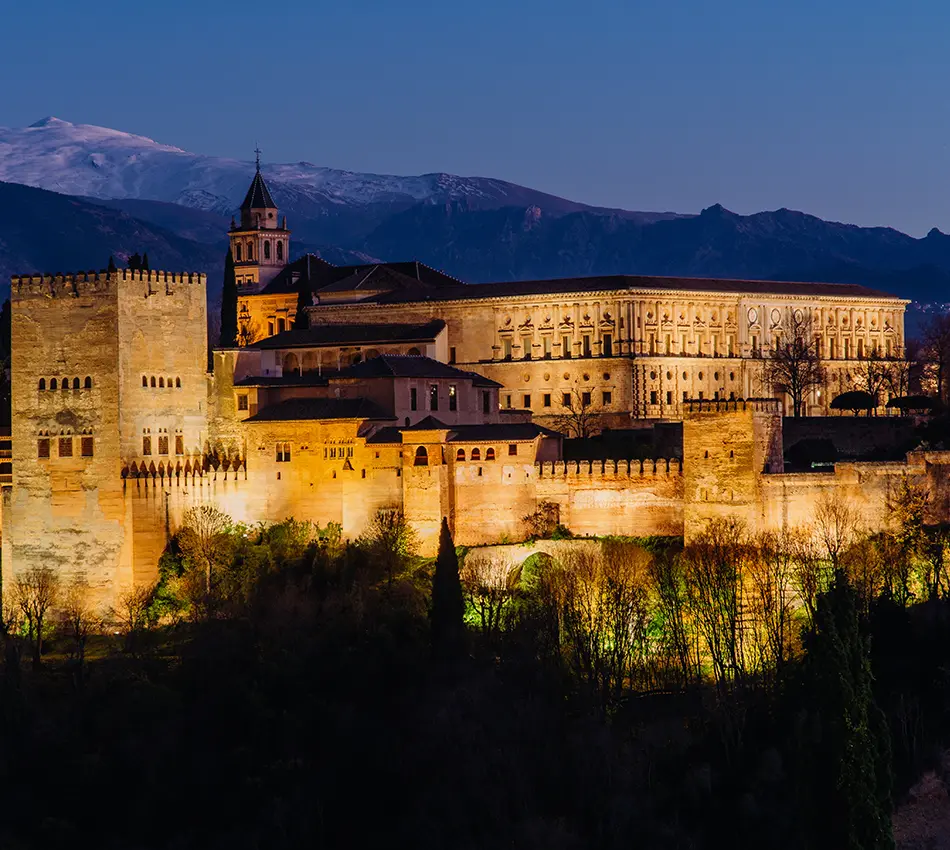 Fortaleza iluminada al atardecer con monta&ntilde;as al fondo.