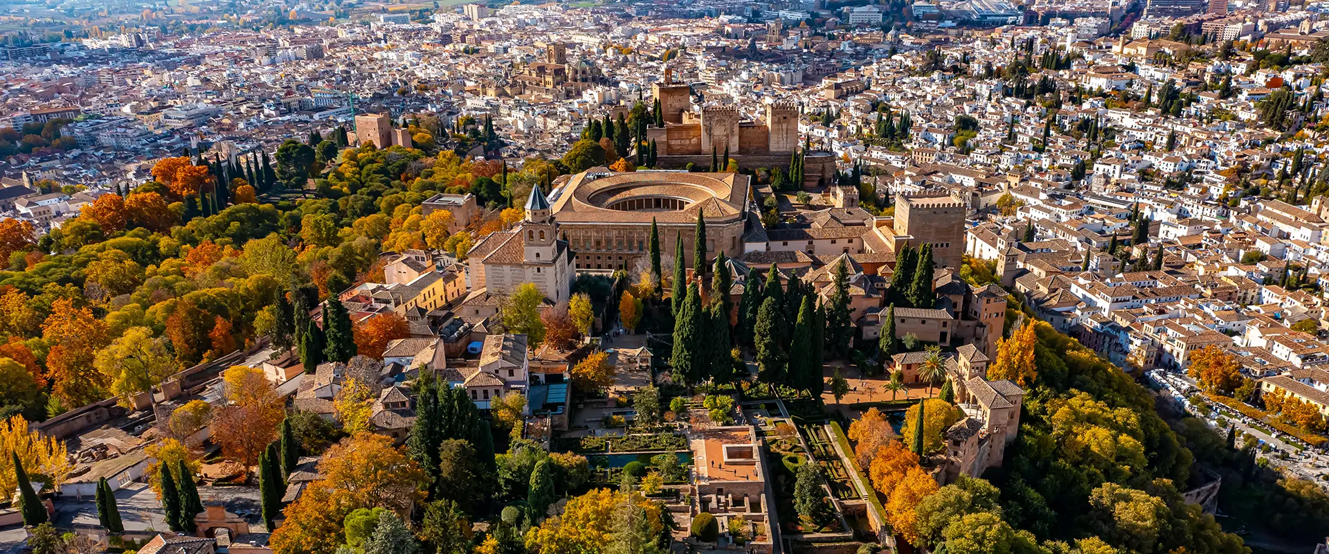 Vista a&eacute;rea de un palacio rodeado de &aacute;rboles y ciudad al fondo en oto&ntilde;o.