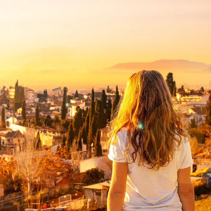Persona mirando un paisaje urbano al atardecer con cielo anaranjado.