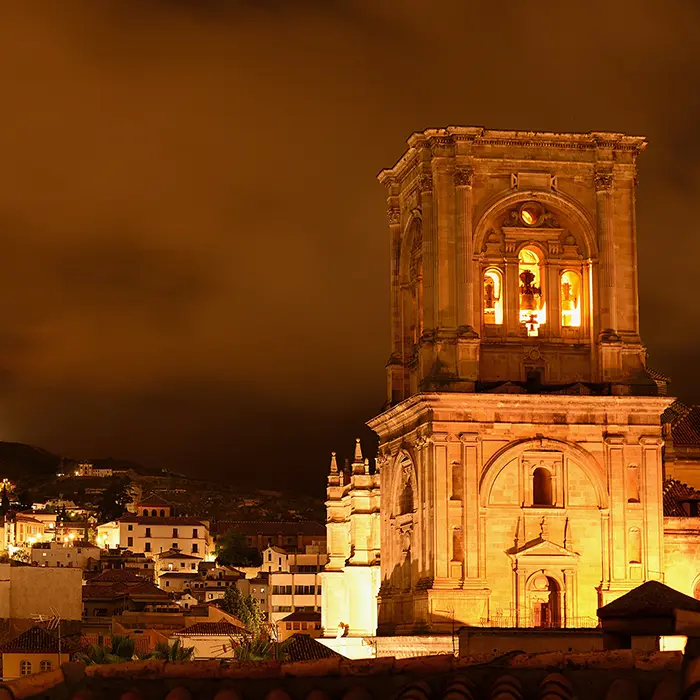 Torre iluminada de una catedral con cielo nocturno nublado al fondo.
