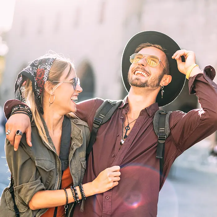 Pareja sonriendo al aire libre con gafas de sol y mochilas.