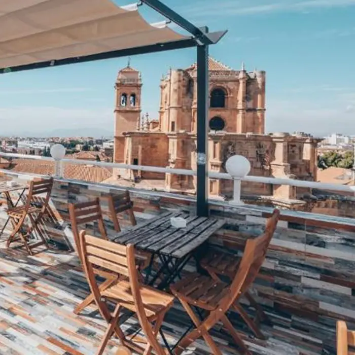 Terraza con muebles de madera y vista a una catedral bajo un cielo despejado.