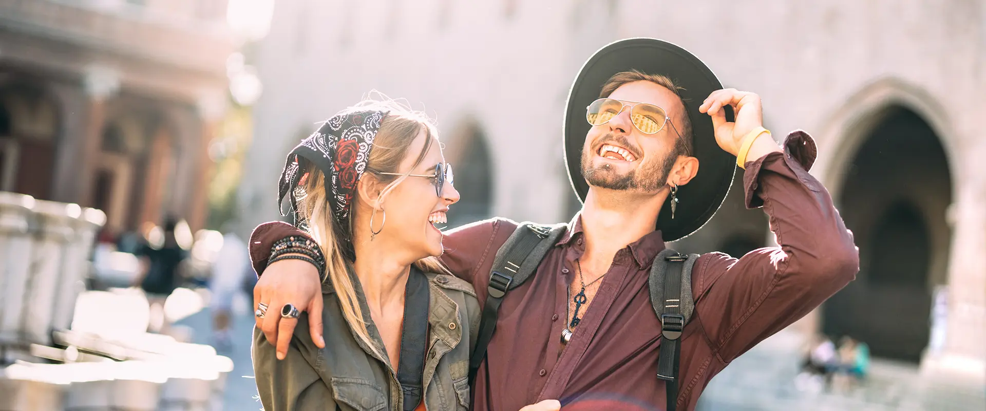 Pareja feliz sonriendo bajo el sol en una plaza hist&oacute;rica.