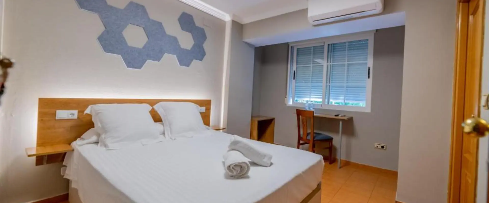 Habitaci&oacute;n luminosa con cama doble, escritorio y ventana.