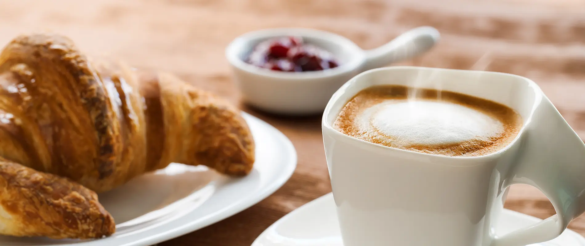 Croissant y capuchino con mermelada en fondo desenfocado.