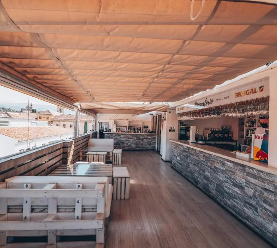 Terraza con p&eacute;rgola y muebles de pal&eacute;s frente a un bar de piedra.