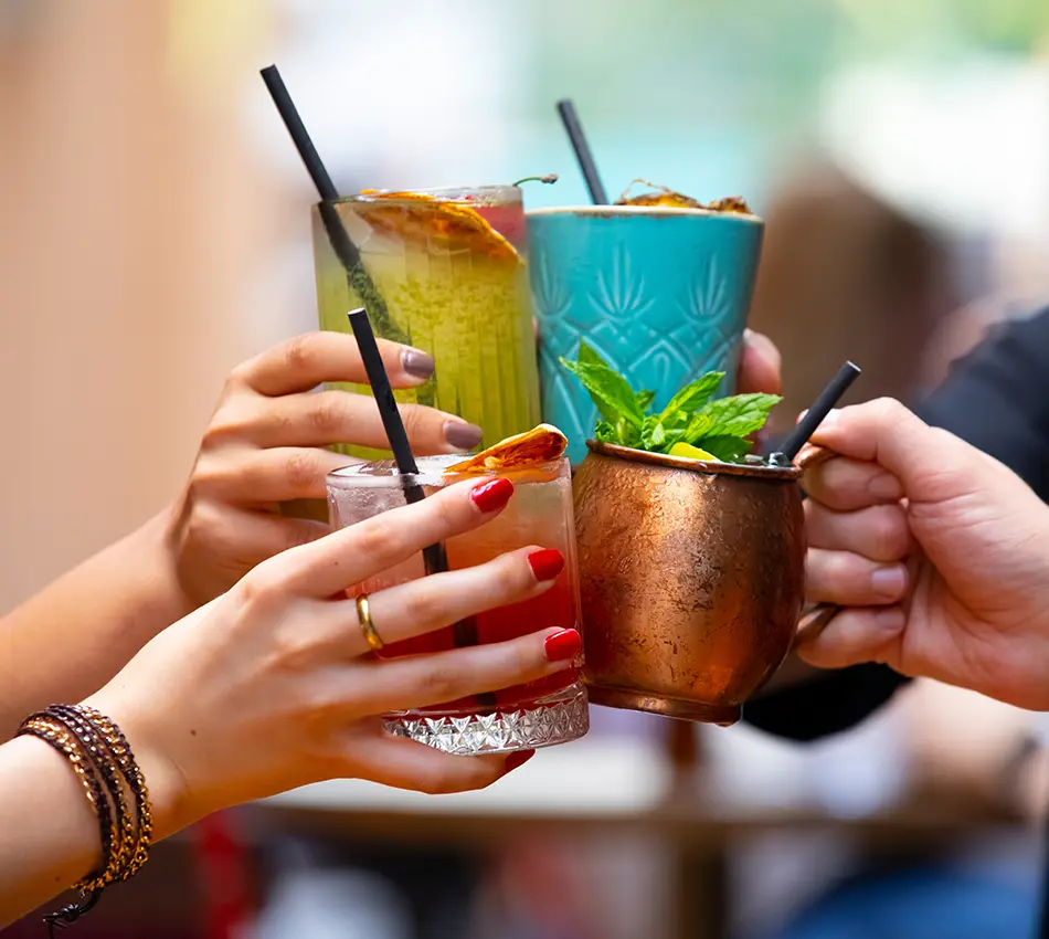 Manos brindando con c&oacute;cteles variados al aire libre.