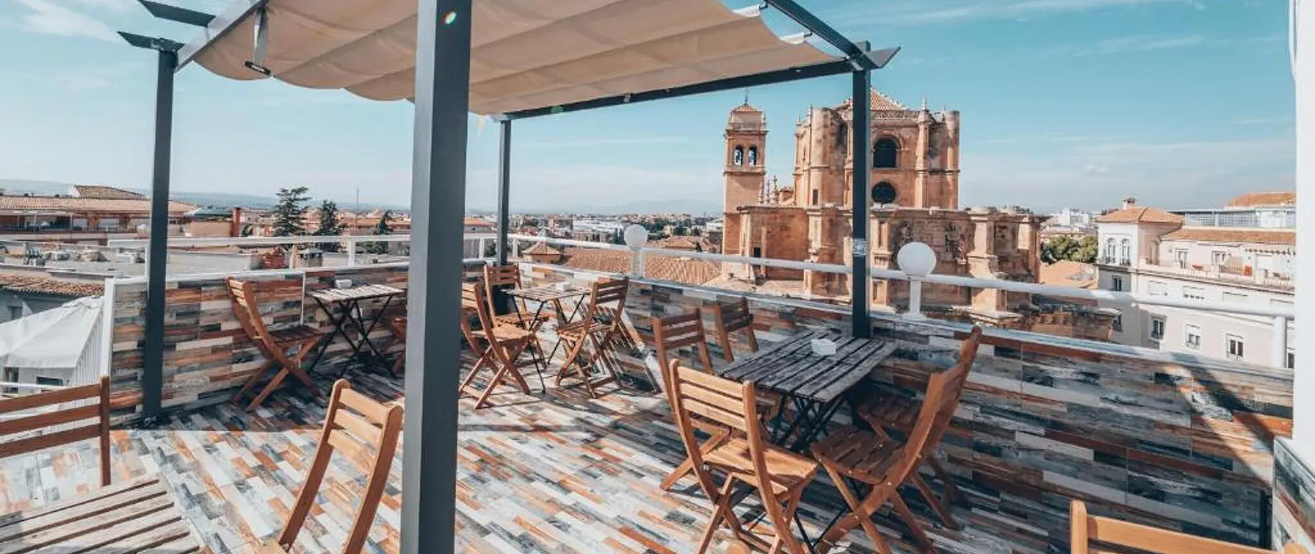 Terraza con mesas y sillas, vista a una iglesia y ciudad al fondo.