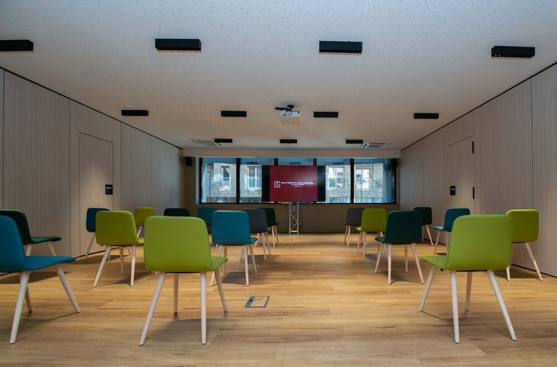 Sala de conferencias vac&iacute;a con sillas coloridas y pantalla al fondo.