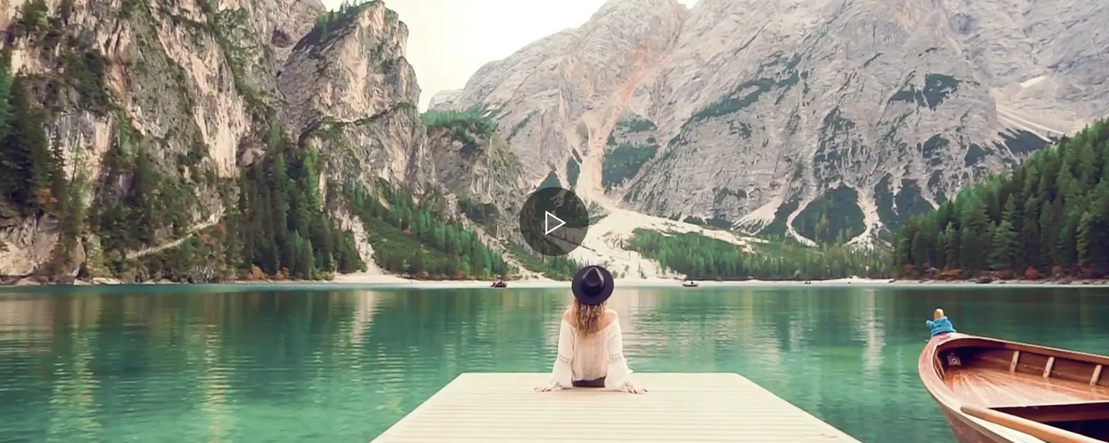 Mujer sentada en muelle frente a un lago y monta&ntilde;as.
