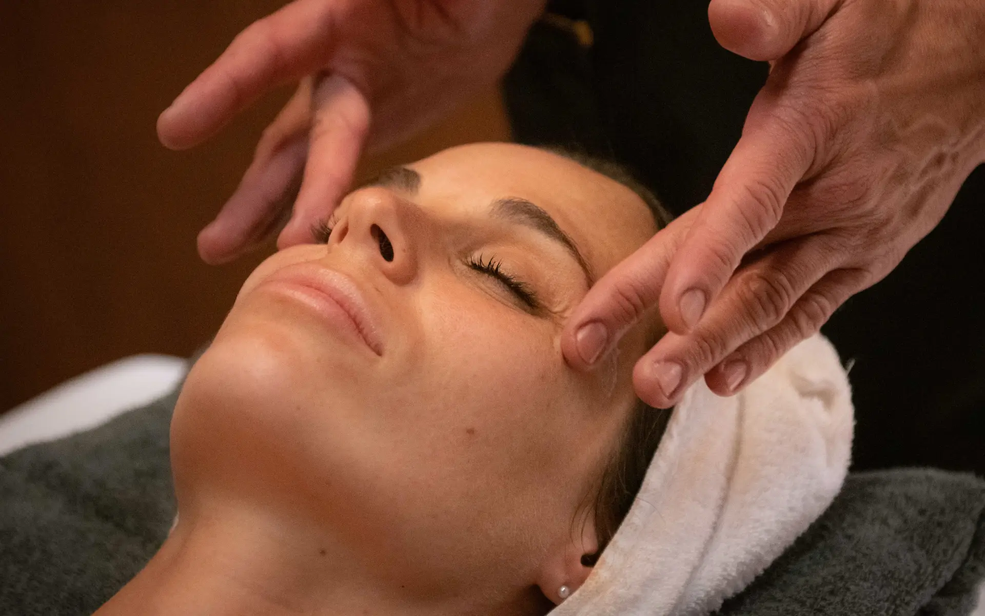 Persona recibiendo un masaje facial, con toalla en la cabeza.