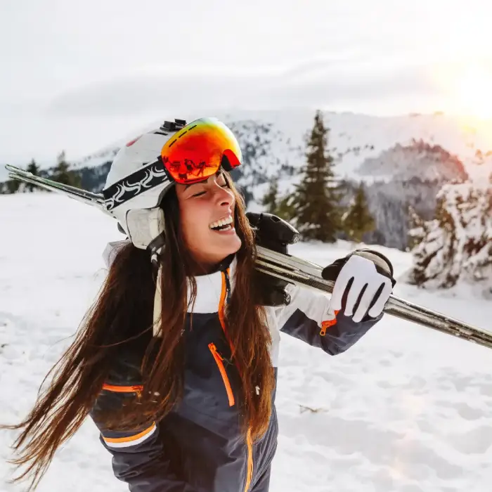Esquiadora sonriente en la nieve con esqu&iacute;s al hombro y gafas anaranjadas.