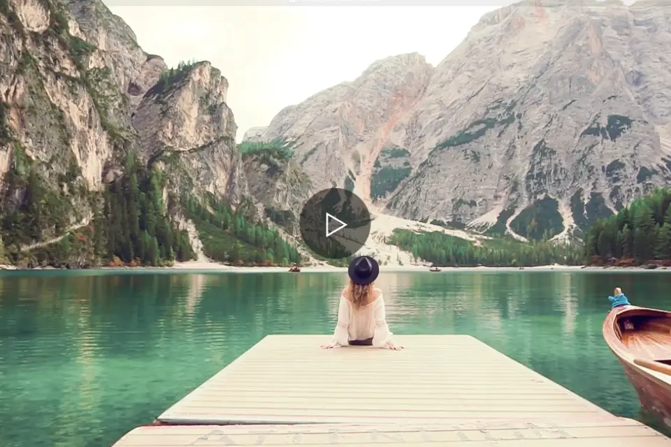 Mujer sentada en un muelle frente a un lago rodeado de monta&ntilde;as.