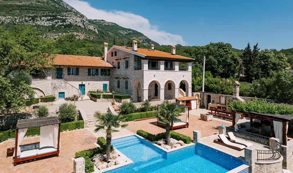 Casa de piedra con piscina y jard&iacute;n, rodeada de monta&ntilde;as y &aacute;rboles.