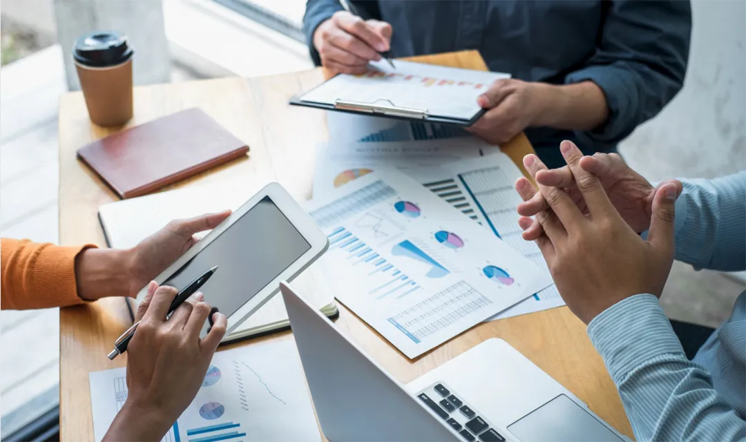 Reuni&oacute;n de trabajo con gr&aacute;ficos y dispositivos en mesa de madera.