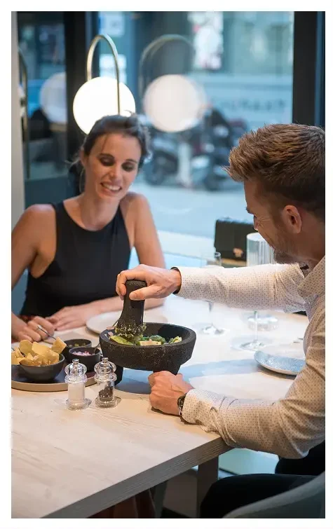 Hombre preparando guacamole en un restaurante mientras una mujer observa sonriendo.