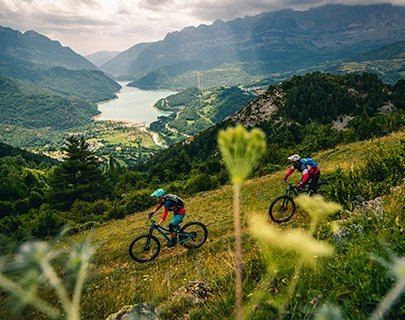 Dos ciclistas recorren un sendero monta&ntilde;oso con vista a un lago y monta&ntilde;as.