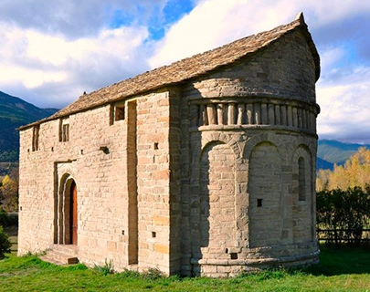 Iglesia rom&aacute;nica de piedra con fondo de monta&ntilde;as y cielo azul.