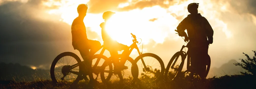 Tres ciclistas al atardecer en una colina.